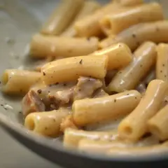 Primo piatto di pasta con guanciale croccante e crema al pecorino romano, un classico saporito.