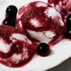 Delizioso gelato al vino con striature rosse e bianche, guarnito con ciliegie scure su un piatto bianco.