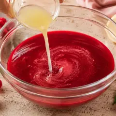 Si aggiunge succo di limone al rosso sciroppo di lamponi fatto in casa da Benedetta, pronto per essere gustato.