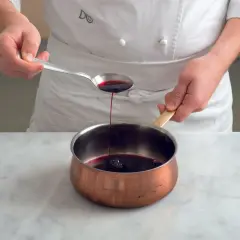 Chef versa un cucchiaio di riduzione di vino rosso in una pentola di rame.