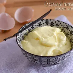 Crema al mascarpone senza uova, soffice e vellutata, servita in una ciotola decorata con un baccello di vaniglia. Guscio d'uovo sullo sfondo.