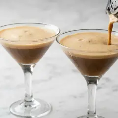 Due bicchieri di caffè shakerato con schiuma cremosa, uno viene riempito da uno shaker.