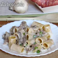 Piatto di pasta alla boscaiola con funghi, piselli e salsiccia, servita su un piatto bianco con un tovagliolo di juta.