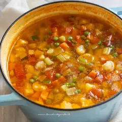 Un fumante minestrone di verdure in una pentola azzurra, ricco di carote, zucchine, piselli e cavolfiore.