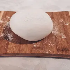 Palla di pasta di zucchero bianca su tagliere di legno, pronta per essere modellata.