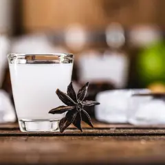 Un bicchierino di cocktail con la sambuca, guarnito con anice stellato, cubetti di ghiaccio e una fetta di lime sullo sfondo.