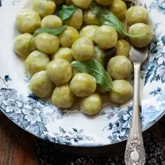 Gnocchi di zucchine soffici e profumati, guarniti con foglie di salvia fresca su un piatto decorato.