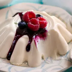 Deliziosa panna cotta con frutti di bosco e salsa ai mirtilli, servita su un piatto decorato.