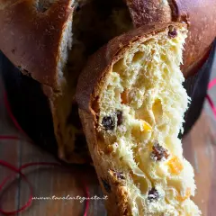 Un dolce panettone casalingo, soffice e profumato, con canditi e uvetta. Una fetta mostra la sua morbidezza e il colore dorato.