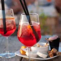 Due cocktail rossi con ghiaccio e arancia, accompagnati da stuzzichini. Perfetti per un aperitivo, ecco la pirlo bianco ricetta.
