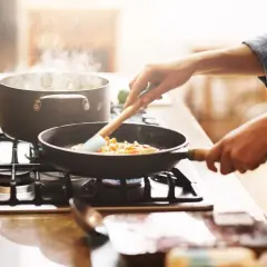 Mani che mescolano verdure in padella, mentre l'acqua bolle in pentola. Un'immagine che evoca il **macerare significato** in cucina: preparare ingredienti con cura.