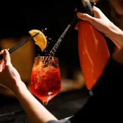 Un barista prepara un Pirlo Spritz, spruzzando acqua frizzante su una fetta d'arancia che decora il bicchiere.