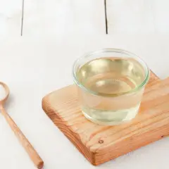 Un cucchiaio di zucchero e un bicchiere di sciroppo di zucchero su un tagliere di legno.