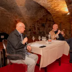 Due uomini discutono del metodo champagne in una cantina storica, con bicchieri da degustazione pronti.