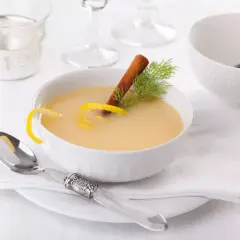 Una ciotola di cremosa salsa al vino bianco, guarnita con scorza di limone, cannella e aneto. Servita con un cucchiaio d'argento.