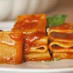 Un primo piatto invitante: paccheri conditi con un sugo rosso vivace, un classico della **pasta allo scarpariello**, guarnito con basilico fresco.