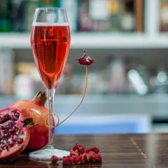 Un bicchiere di tintoretto cocktail rosso rubino, accompagnato da melograni freschi e secchi, su un tavolo di legno scuro.