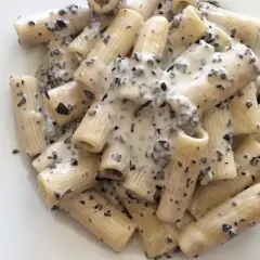 Rigatoni conditi con una cremosa salsa bianca e pezzetti scuri, un invitante piatto di pasta alla cenere.