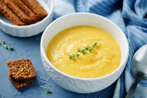 Una ciotola di cremosa salsa di ceci, guarnita con timo, accanto a fette di pane integrale e un tovagliolo blu a righe.