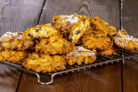 Un mucchio di croccanti biscotti alle corn flakes e uvetta, spolverati di zucchero a velo, sembrano piccole rose del deserto su una griglia.