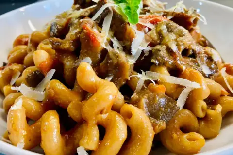 Un piatto invitante di pasta alla norma con melanzane, pomodoro e ricotta salata grattugiata, guarnito con basilico fresco.