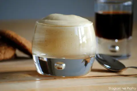 Delizioso zabaione ricetta in un bicchiere, con biscotti e caffè sullo sfondo.