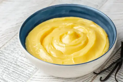 Una ciotola blu piena di soffice crema pasticcera, con baccelli di vaniglia scuri accanto.
