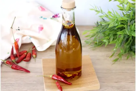 Una bottiglia di olio al peperoncino, con peperoncini rossi secchi sparsi intorno e un tocco di verde sullo sfondo.