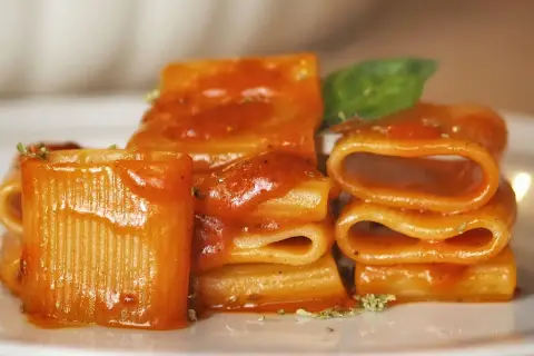 Un primo piatto invitante: paccheri conditi con un sugo rosso vivace, un classico della **pasta allo scarpariello**, guarnito con basilico fresco.