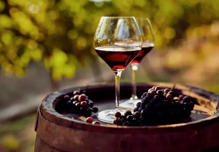 Due calici di vino rosso e grappoli d'uva su una botte. Un'immagine che evoca il processo di come si fa il vino novello.