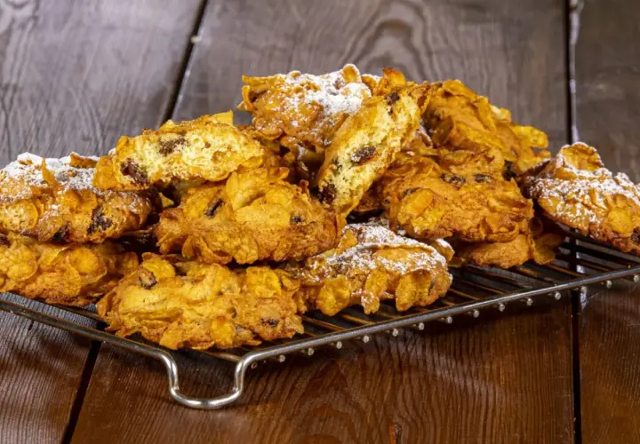 Un mucchio di croccanti biscotti alle corn flakes e uvetta, spolverati di zucchero a velo, sembrano piccole rose del deserto su una griglia.