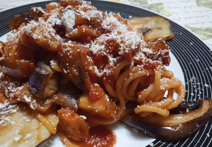 Un piatto invitante di pasta con melanzane, condita con sugo rosso e abbondante formaggio grattugiato.