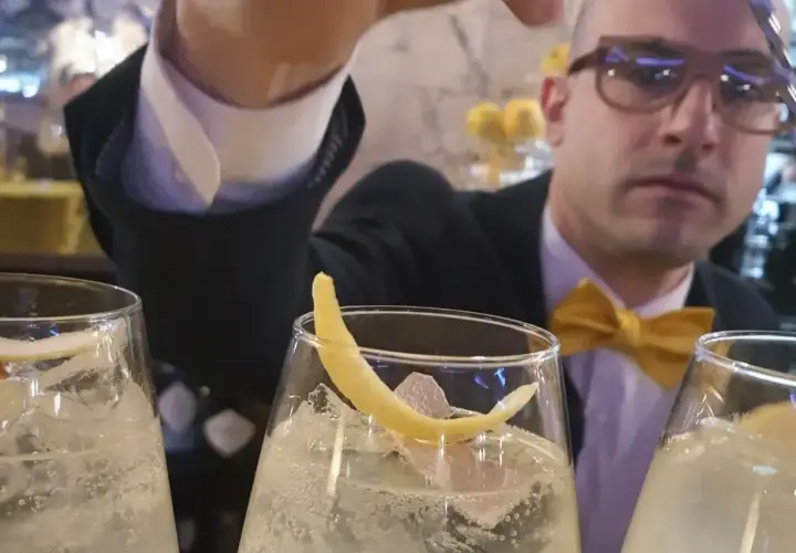 Un barista con papillon giallo prepara un bergamotto spritz, guarnito con scorza di limone.