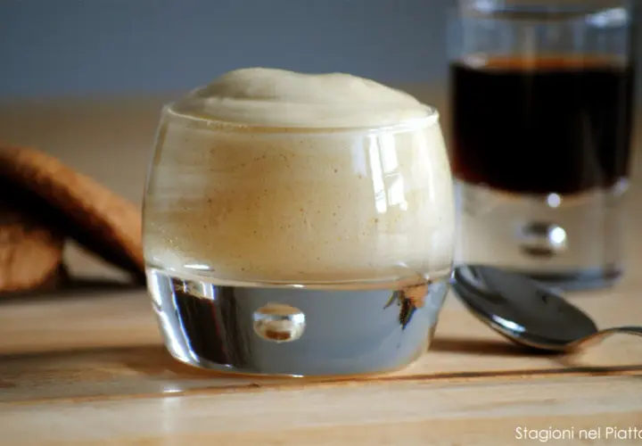 Delizioso zabaione ricetta in un bicchiere, con biscotti e caffè sullo sfondo.