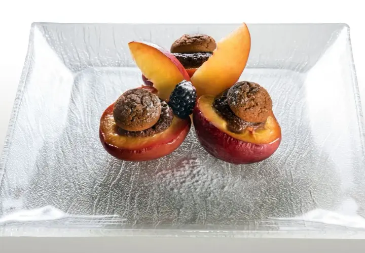 Deliziose pesche ripiene alla piemontese, guarnite con amaretti e frutti di bosco, su un piatto di vetro.