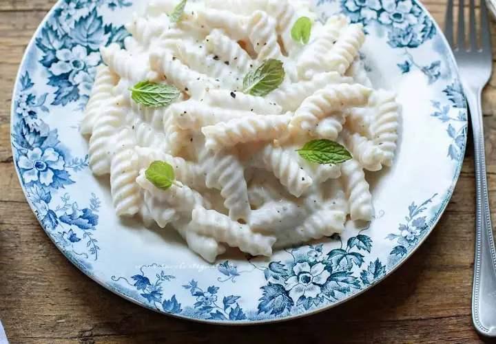 Fusilli cremosi con un sugo leggero alla ricotta, guarniti con foglie di menta fresca su un piatto decorato.