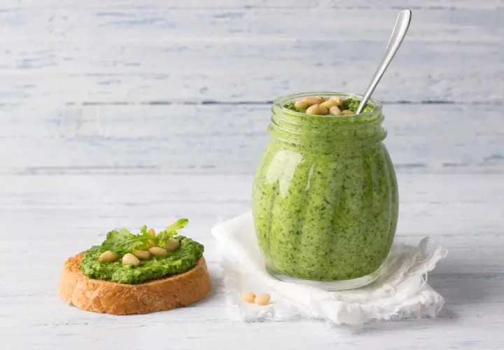 Pesto di rucola ricetta: un vasetto pieno di verde brillante e una bruschetta guarnita, pronti per essere gustati.