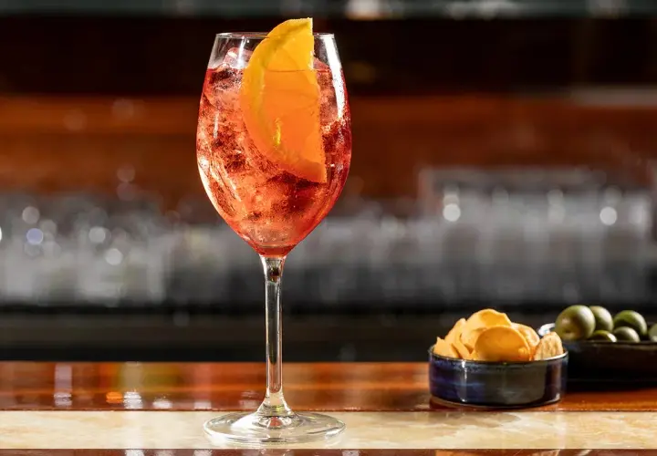 Un rinfrescante cocktail spritz, con una fetta d'arancia e ghiaccio, servito su un bancone di legno lucido.