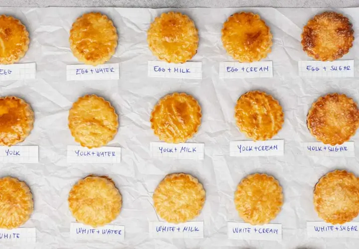 Quindici pasticcini dorati, ognuno con un'etichetta che indica il tipo di egg wash usato per ottenere la sua lucentezza.
