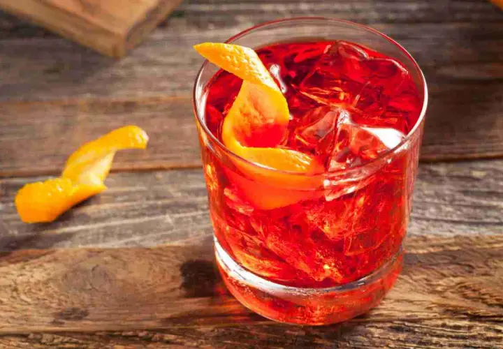 Un Negroni Sbagliato, con la sua vibrante gradazione di rosso, servito con ghiaccio e una scorza d'arancia su un tavolo di legno.