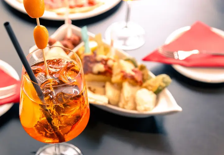 Un bicchiere di spritz aperitivo con amici, ghiaccio e arancia, accompagnato da stuzzichini.