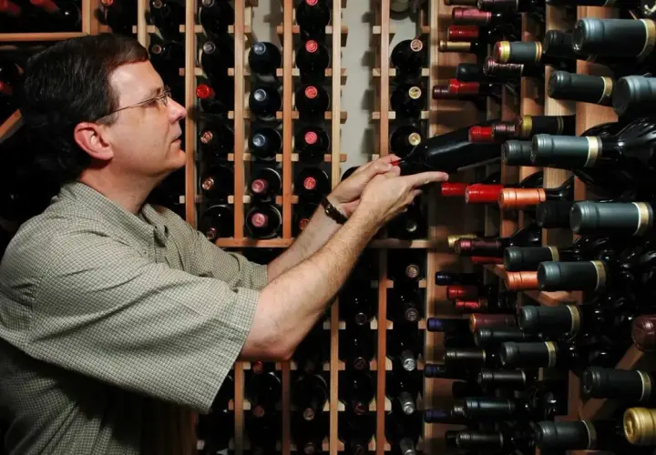 Un uomo sceglie tra una vasta cantina di cru vini, selezionando attentamente una bottiglia.