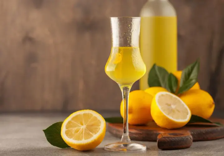 Un bicchiere di limoncello, frutto di un processo di limoncello scientifico, con limoni freschi e una bottiglia sullo sfondo.