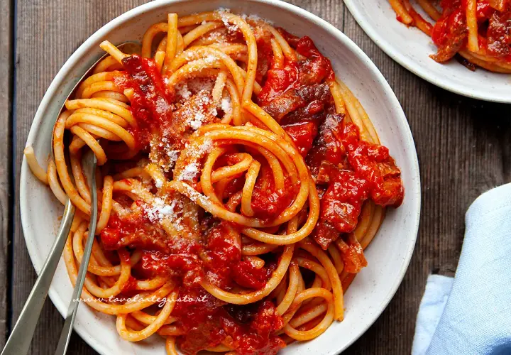 Un piatto invitante di bucatini all'amatriciana ricetta, conditi con sugo rosso e guanciale croccante, spolverati di pecorino.