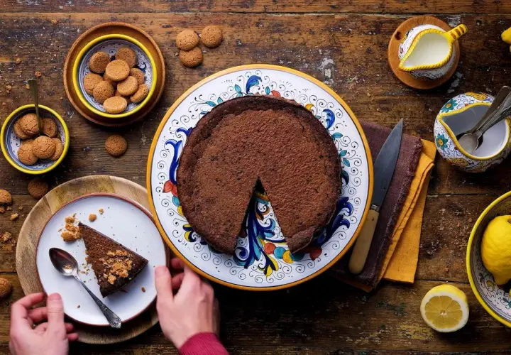 La crescionda spoletina ricetta originale, una torta al cioccolato scuro su un piatto decorato, con amaretti e limoni freschi.