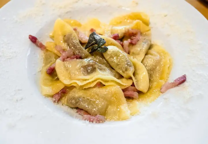 Piatto di casoncelli alla bergamasca con pancetta e salvia, spolverati di formaggio grattugiato.