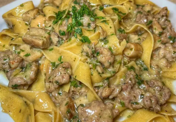 Pappardelle cremose con un saporito sugo di pasta salsiccia e funghi, guarnite con prezzemolo fresco.