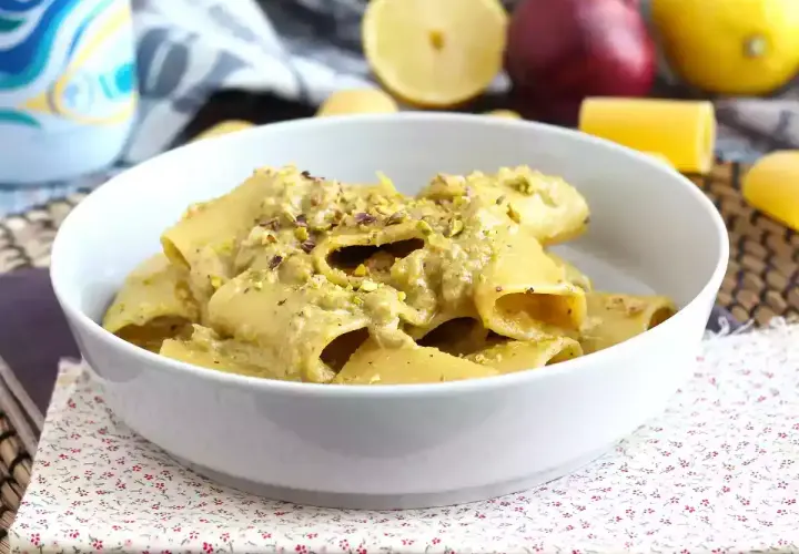 Piatto di pasta tonno e limone, condita con una crema verde e pistacchi tritati, servita in una ciotola bianca.