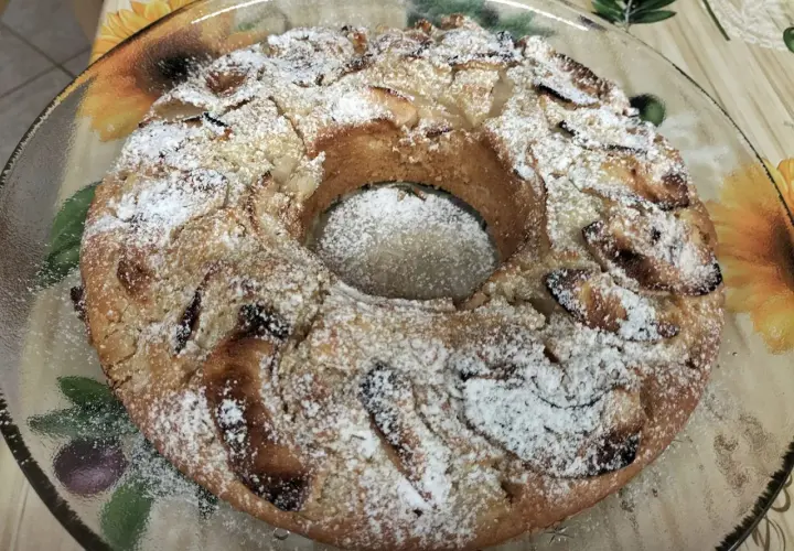 Torta all'acqua soffice e profumata, cosparsa di zucchero a velo, con pezzi di mela visibili.