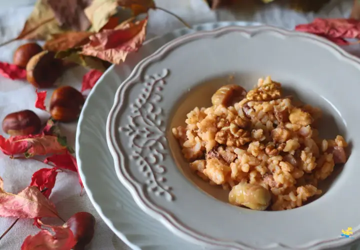 Un cremoso risotto castagne e gorgonzola, guarnito con noci e castagne intere, su un piatto decorato, circondato da foglie autunnali e castagne.